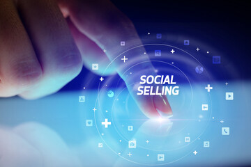 Finger touching tablet with social media icons and SOCIAL SELLING