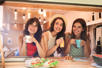 Happy young women having breakfast in trailer. Camping vacation