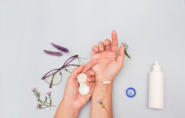 Female hands hold a container with contact lenses. Contact lenses in hand. Lenses, container, glasses on a blue background with flowers. eye health concept, optics. Ophthalmologist tools.