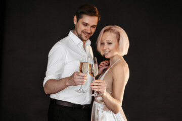 Beautiful happy couple young family in evening dresses with glasses of champagne on dark background