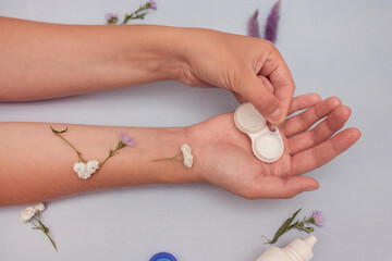 Female hands hold a container with contact lenses. Contact lenses in hand. Lenses, container, glasses on a blue background with flowers. eye health concept, optics. Ophthalmologist tools.