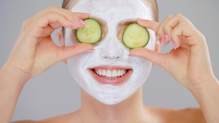 Extreme Clouseup Portrait Young Caucasian Beautiful Blonde Woman With Blue Eyes She Covering Eye Fresh Cucumber White Mask Cosmetic On Face And Smiling On Gray Background Skin Care Concept