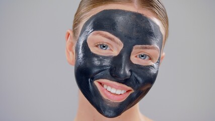 Clouse-up Portrait Young Caucasian Beautiful Blonde Woman With Blue Eyes And Black Mask Cosmetic On Face And Smiling On Gray Background Skin Care Concept
