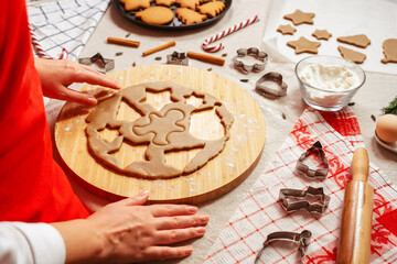 Woman baker cutting cookies from raw gingerbread dough. Close up side view of home kitchen table in preparation. New Year holidays concept.