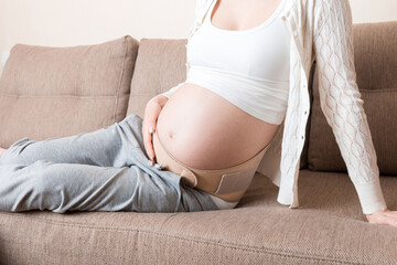 Pregnant womanlying on sofa in abdominal support bandage. Maternity healthcare concept support...