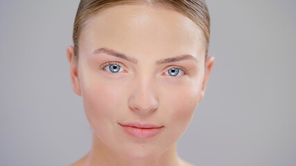 Fototapeta premium Close Up Beautiful Young Caucasian Blonde Woman With Blue Eyes And Smooth Healthy Skin Looking To The Camera And Smiling Skin Care Cosmetic Concept
