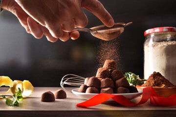 Hands pouring cocoa powder on freshly made chocolate truffles
