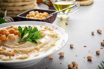 Low angle view at Hummus topped with chickpeas, olive oil and green coriander leaves on stone table with pita bread aside