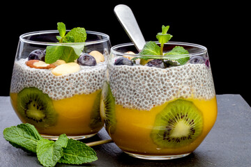 
pudding with chia, mango and kiwi seeds in a glass glass, selective focus. On a black background
