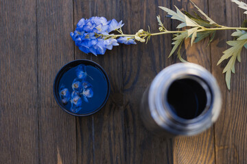 Thermos with tea and a purple flower on the background of nature and a fence. Stop in the journey. Wood texture
