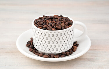 Coffee beans in a white ceramic Cup and saucer on a light background. Side view. Concept of coffee backgrounds.