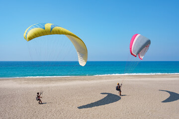 Paraglider tandem flying over the sea shore with blue water and sky on horison. View of paraglider...