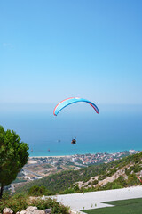 Orange paraglider flies over a mountain valley on a sunny summer day. Paragliding in the mountains in the sky