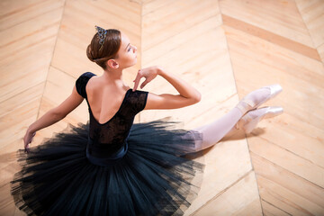 Fototapeta premium ballerina in a black tutu sitting on floor with her back to the camera.