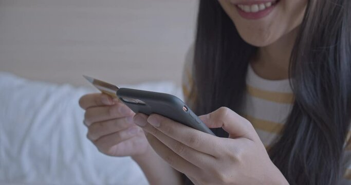 Happy young woman asian are shopping online by smartphone and credit card in bed room.