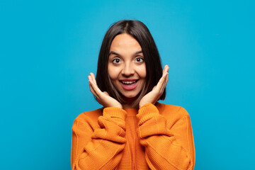 hispanic woman feeling shocked and excited, laughing, amazed and happy because of an unexpected...