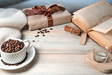 A mug with coffee beans, a gift box, a book, a sweater on a wooden table, with space for copying. Side view.