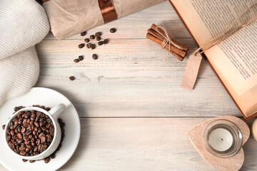 Cozy background with coffee beans in a white Cup, sweater, book, gift on a light wooden table. The view from the top.