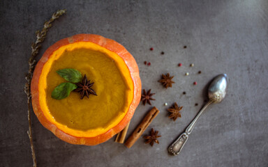 Spicy squash soup in pumpkin bowl. Top view photo on grey table. Winter receipts. 