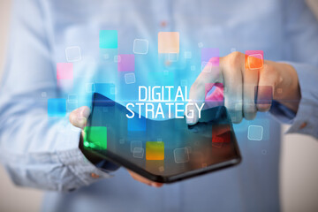 Young man holding a foldable smartphone with DIGITAL STRATEGY inscription, educational concept