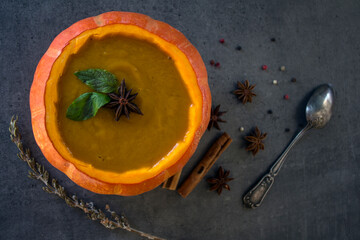 Spicy squash soup in pumpkin bowl. Top view photo on grey table. Winter receipts. 