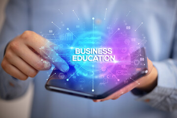 Businessman holding a foldable smartphone with BUSINESS EDUCATION inscription, new business concept