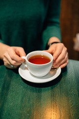 A cup of tea in hands on a green wooden table