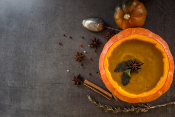 Spicy squash soup in pumpkin bowl. Top view photo on grey table. Winter receipts. 