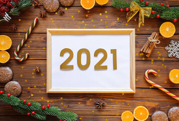 new year party preparation frame with orange, tangerine, gingerbread and spices, decoration, fir tree, sparkles and cones on wooden background top veiw. wood frame with gold numbers 2021 in the center