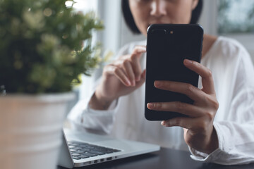 Woman using mobile phone during working on laptop computer from home office