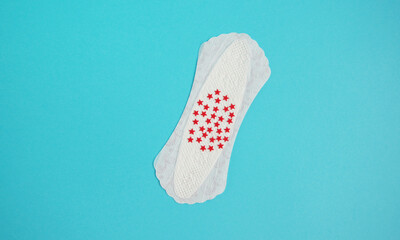 Menstrual female pad with red glitter stars on bright blue background. Menstrual concept.