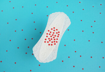 Menstrual female pad with red glitter stars on bright blue background. Menstrual concept.
