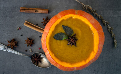 Spicy squash soup in pumpkin bowl. Top view photo on grey table. Winter receipts. 