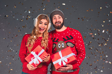 Young couple with christmas presents on grey background.