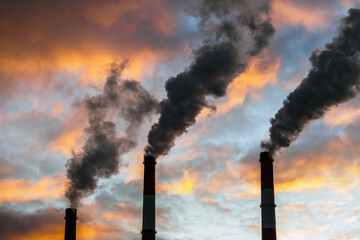 Three Smoking chimneys in dramatic colorful sky background. The concept of air pollution and the...