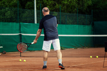 An aged man plays tennis on the court. Active lifestyle and health. Back view.