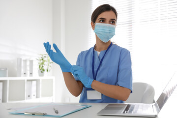 Doctor in protective mask putting on medical gloves at table in office