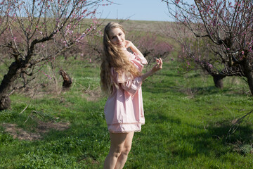Obraz premium Beautiful blonde woman in pink dress walks through the flowering garden
