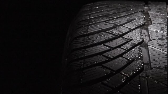 Slow Rotation of a Car Tire. The geometric pattern of the wheel in water droplets slowly rotates towards the viewer. Drops sparkle on the black rubber on a black background