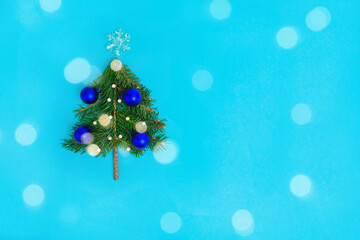 Fototapeta na wymiar Small Christmas tree with blue balls on lturquoise background decorated by christmas lights with bokeh.