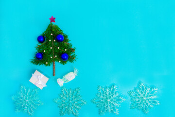 Small Christmas tree decorated with blue balls on turquoise background. Holiday greeting card.