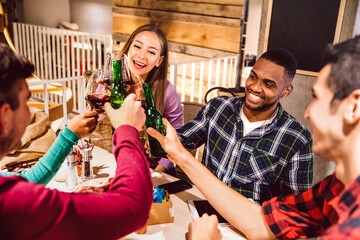 Happy multiracial friends toasting beer indoor at brewery pub - Inclusive friendship lifestyle concept with young people enjoying time and having fun together - Warm filter with focus on eyes