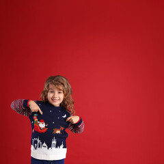 Cute little girl pointing at her Christmas sweater against red background. Space for text