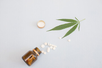 a jar of pills and marijuana. scattered pills from a jar on the table and cannabis on a white background. top view. marijuana leaf
