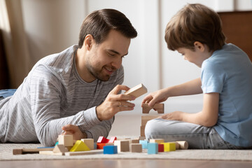 Obraz na płótnie Canvas Close up loving father playing with adorable son at home, sitting on warm floor in living room, happy dad and little boy kid constructing with wooden colorful blocks, enjoying leisure time