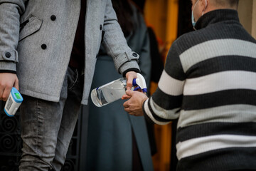 Details with the hands of a man taking the temperature and also disinfecting the hands of people entering a public institution.