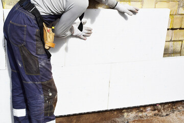 Worker installing white rigid polyurethane foam sheet on building wall facade for energy saving. Diy, house improvement and insulation concept.
