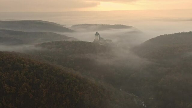 Aerial view of the medieval castle Karlstejn situated on the top of a hill, surrounded by forest in autumn. Valley and forest covered by fog in the morning