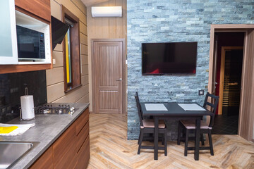 Grey-brown interior of the kitchen. Guest house with kitchen and sauna. The door from the kitchen to the sauna is open. Dining room with TV on the wall.