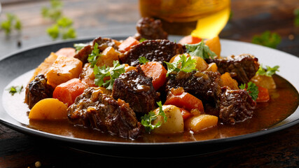 Beef Stew with carrot and baby potato in black plate on wooden table